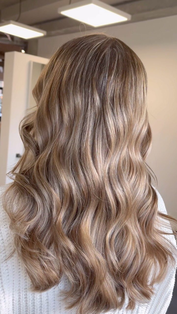 Long sandy blonde waves show subtle fine highlights and darker roots