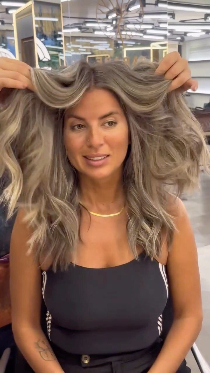 Woman showing long, wavy smoky gray-blonde hair in a salon