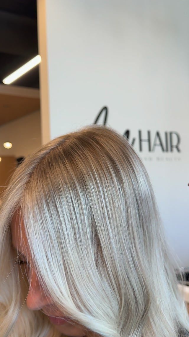 Straight blonde hair with darker roots and cool, pale lengths in a salon