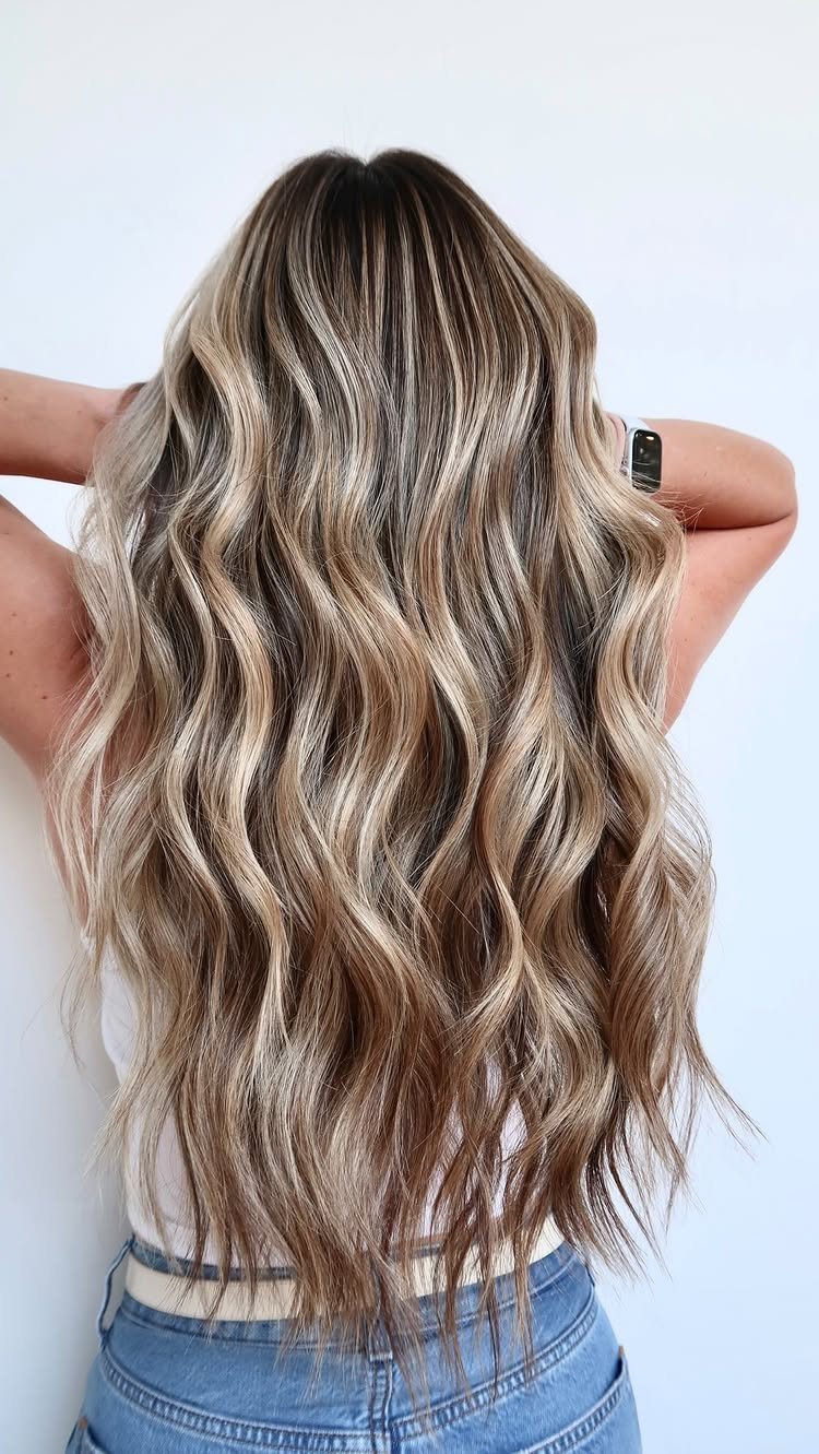 Long wavy blonde hair with dark roots and beige balayage strands