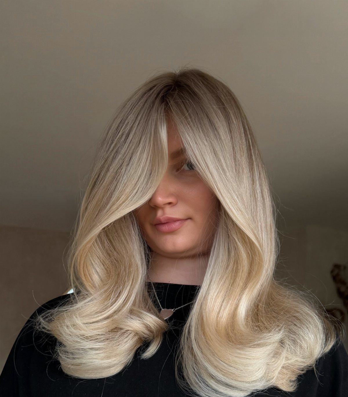 Woman displaying long blonde waves with darker roots and pale golden highlights