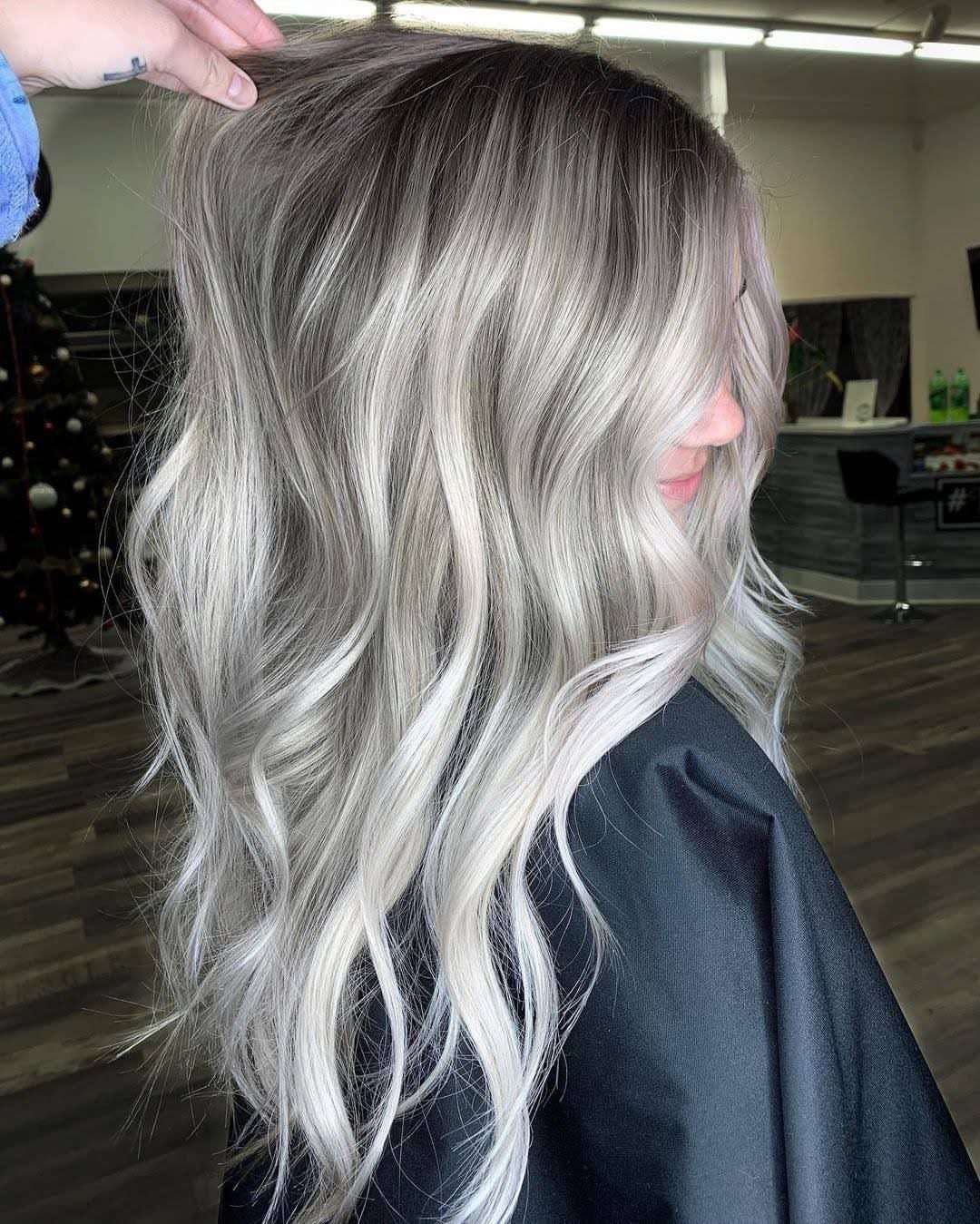 Long wavy icy blonde hair with darker roots shown in a salon