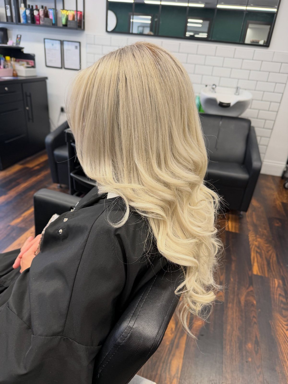 Long pale blonde hair with darker roots and curled icy ends in a salon