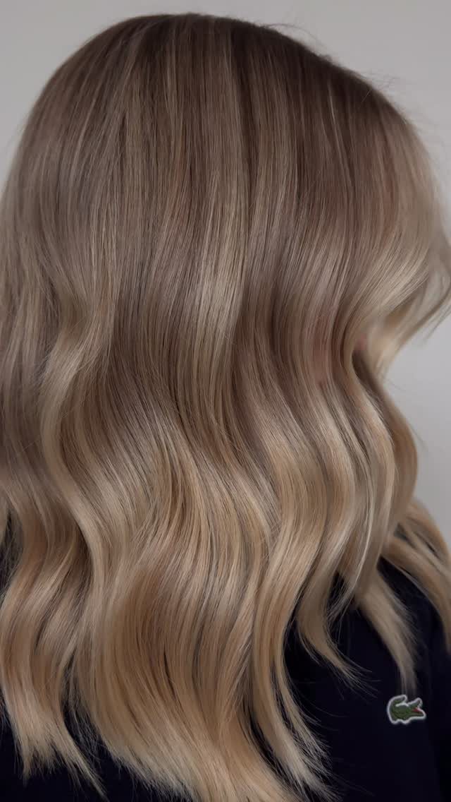 Wavy neutral blonde hair blends dark roots with soft beige lengths