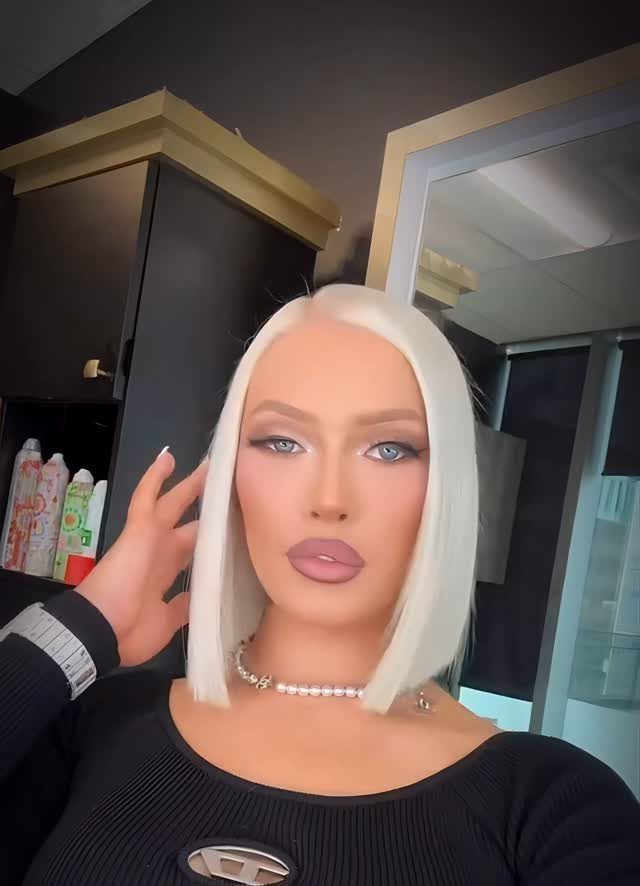 Person posing with an extremely light blonde bob against dark cabinets and a mirror
