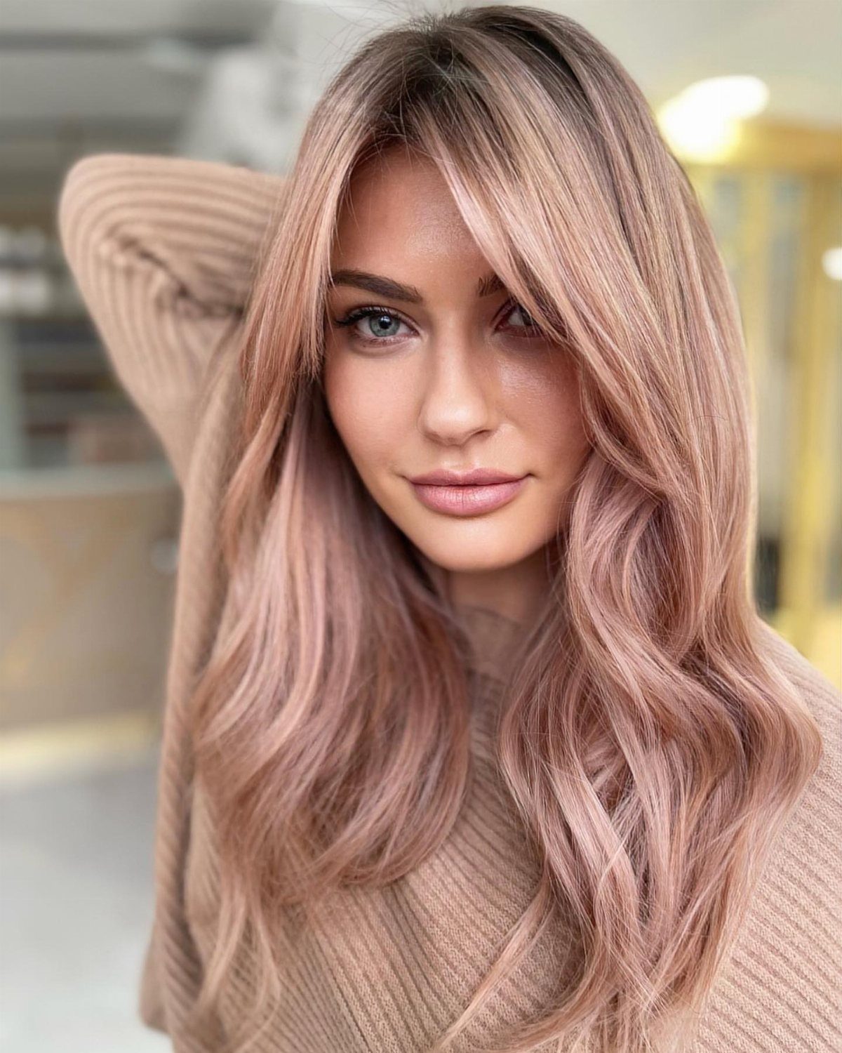 Woman with long rosy blonde waves and darker roots wearing a beige sweater