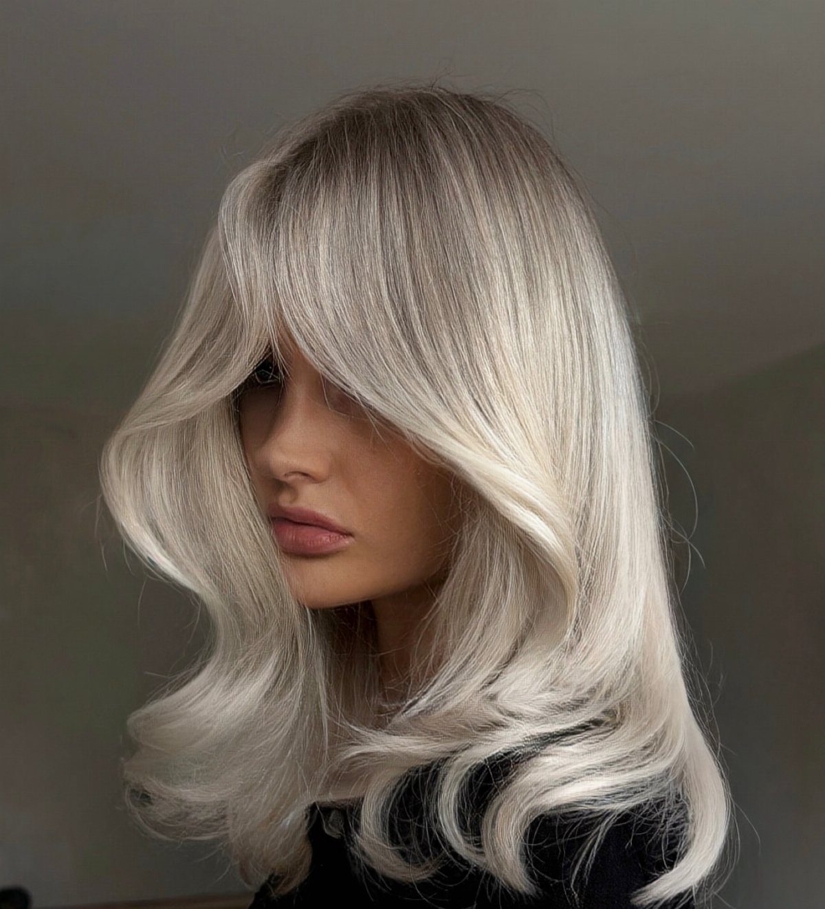 Woman with long silver-white hair, dark roots, and voluminous curled ends