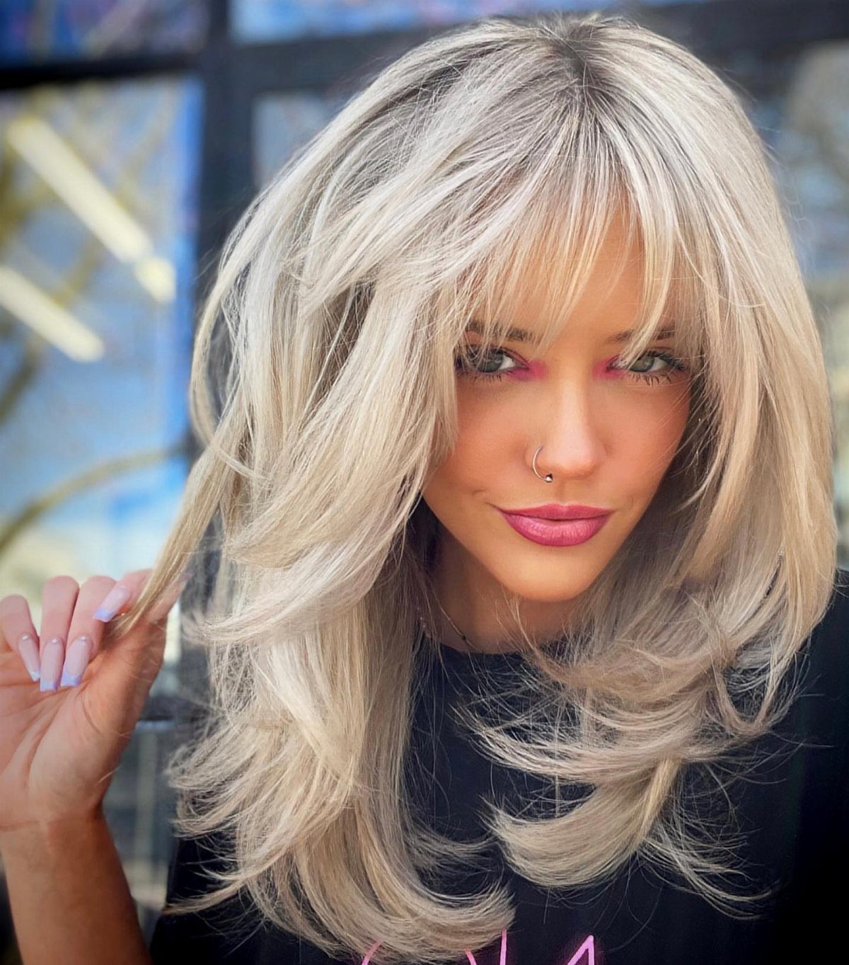 Woman with voluminous light blonde layered hair and curtain bangs posing indoors