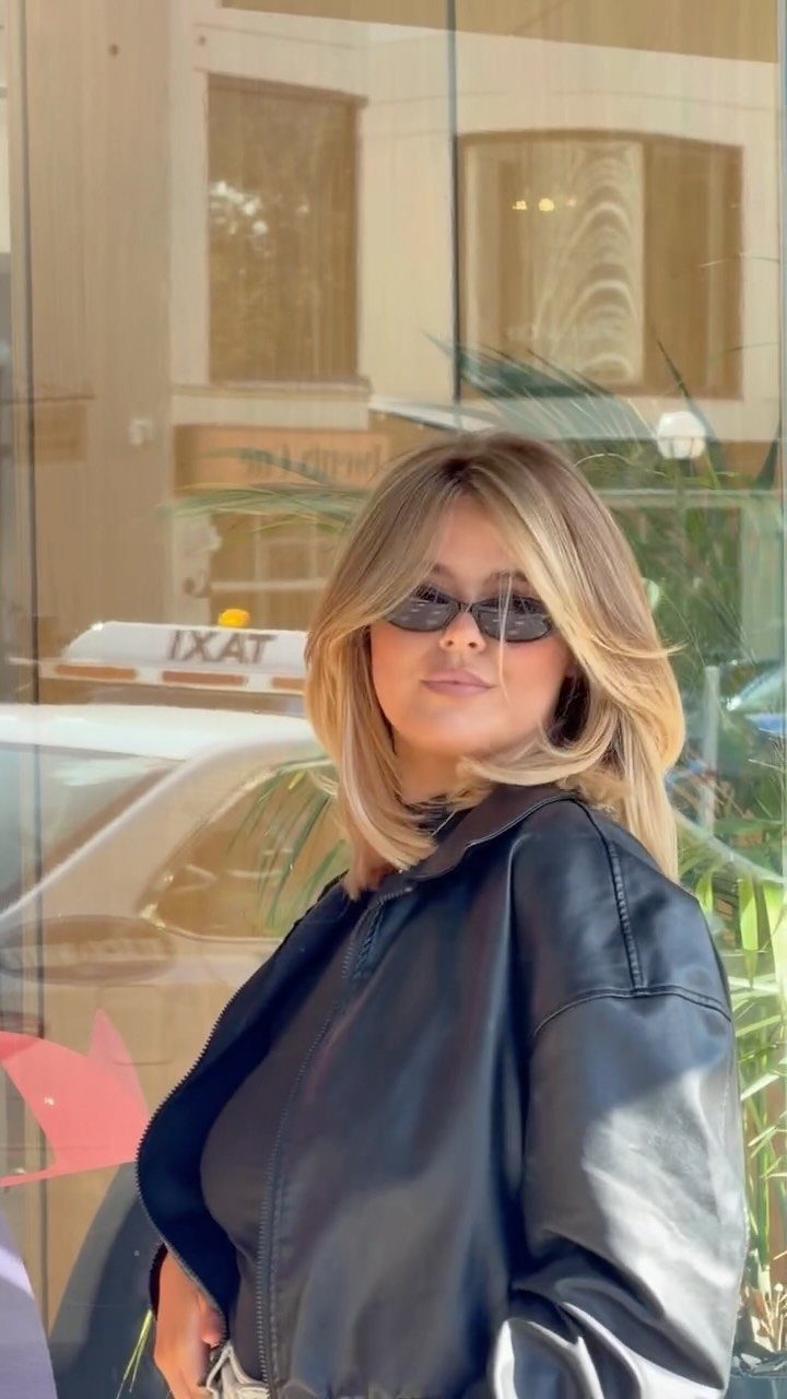 Woman with a short blonde balayage bob, darker roots, sunglasses, and a black leather jacket