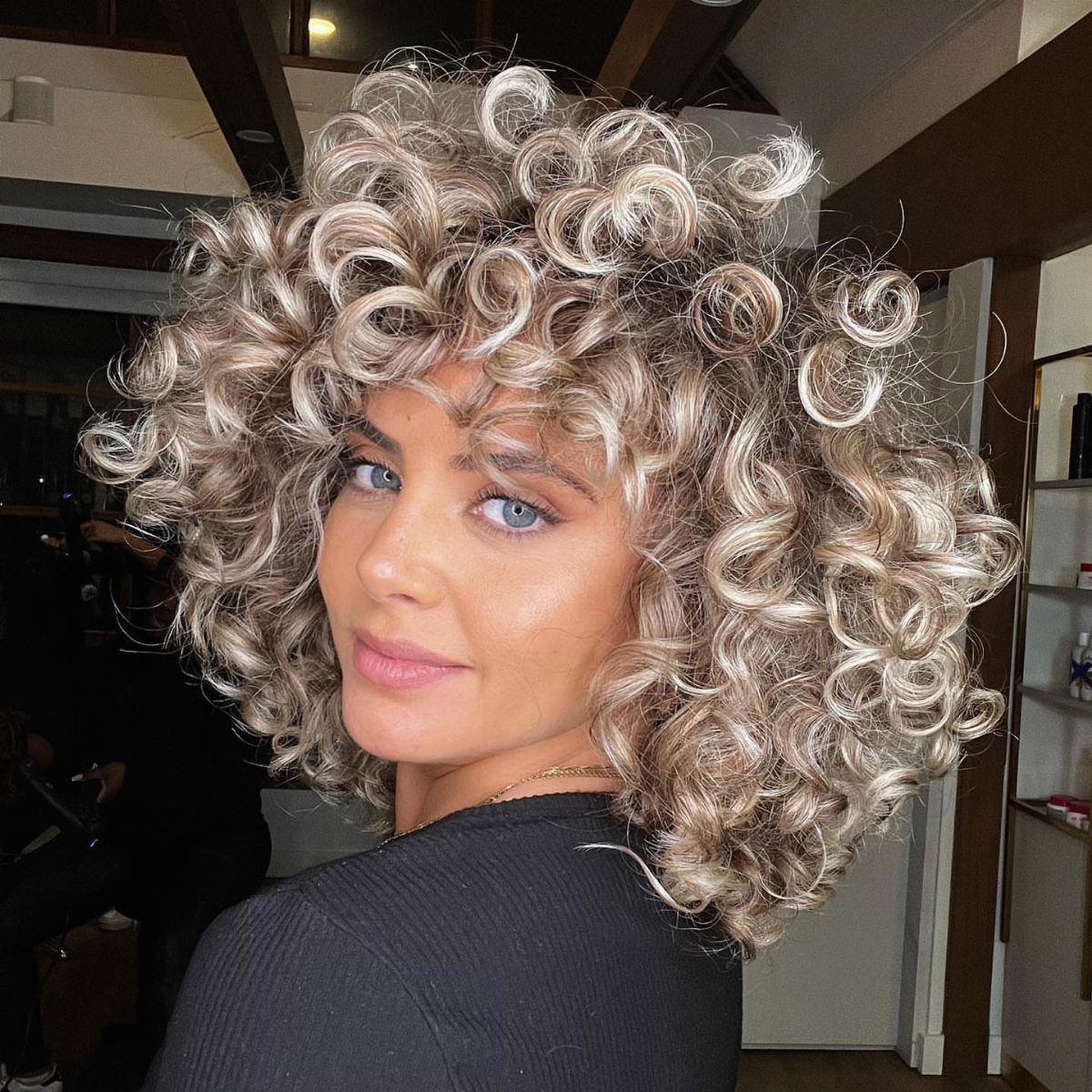 Person posing with voluminous pale blonde spiral curls framing the face