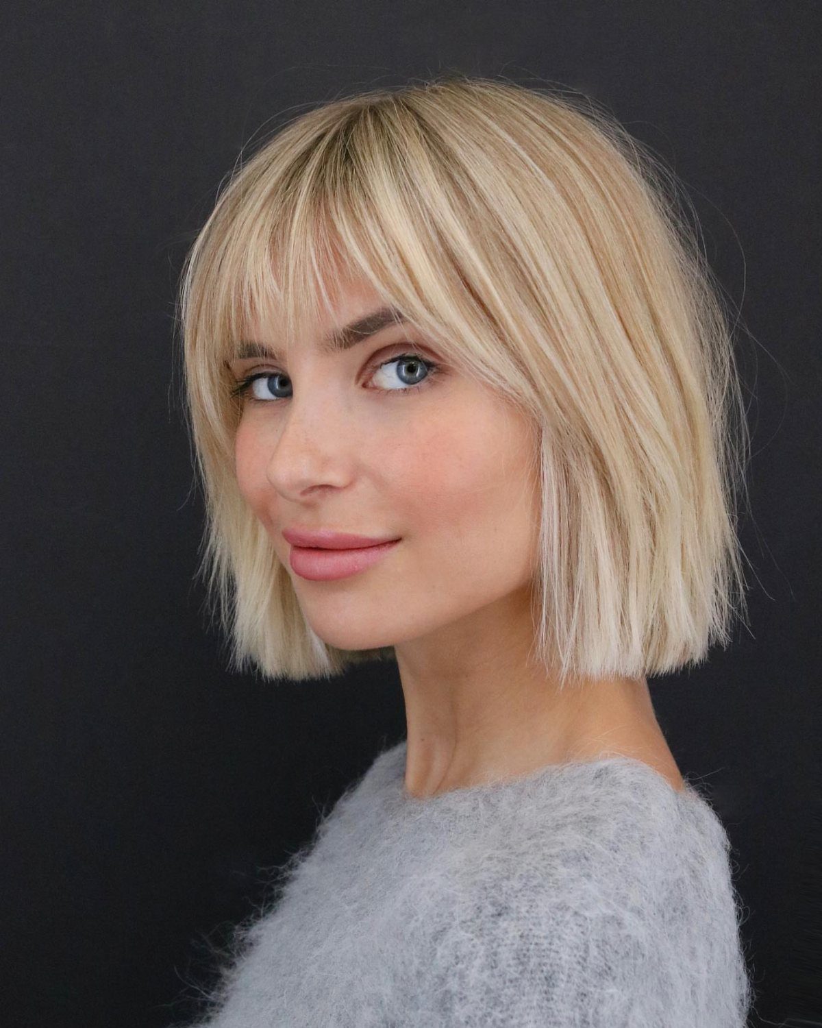 Woman wearing a short blonde bob with center-parted curtain bangs against a dark background