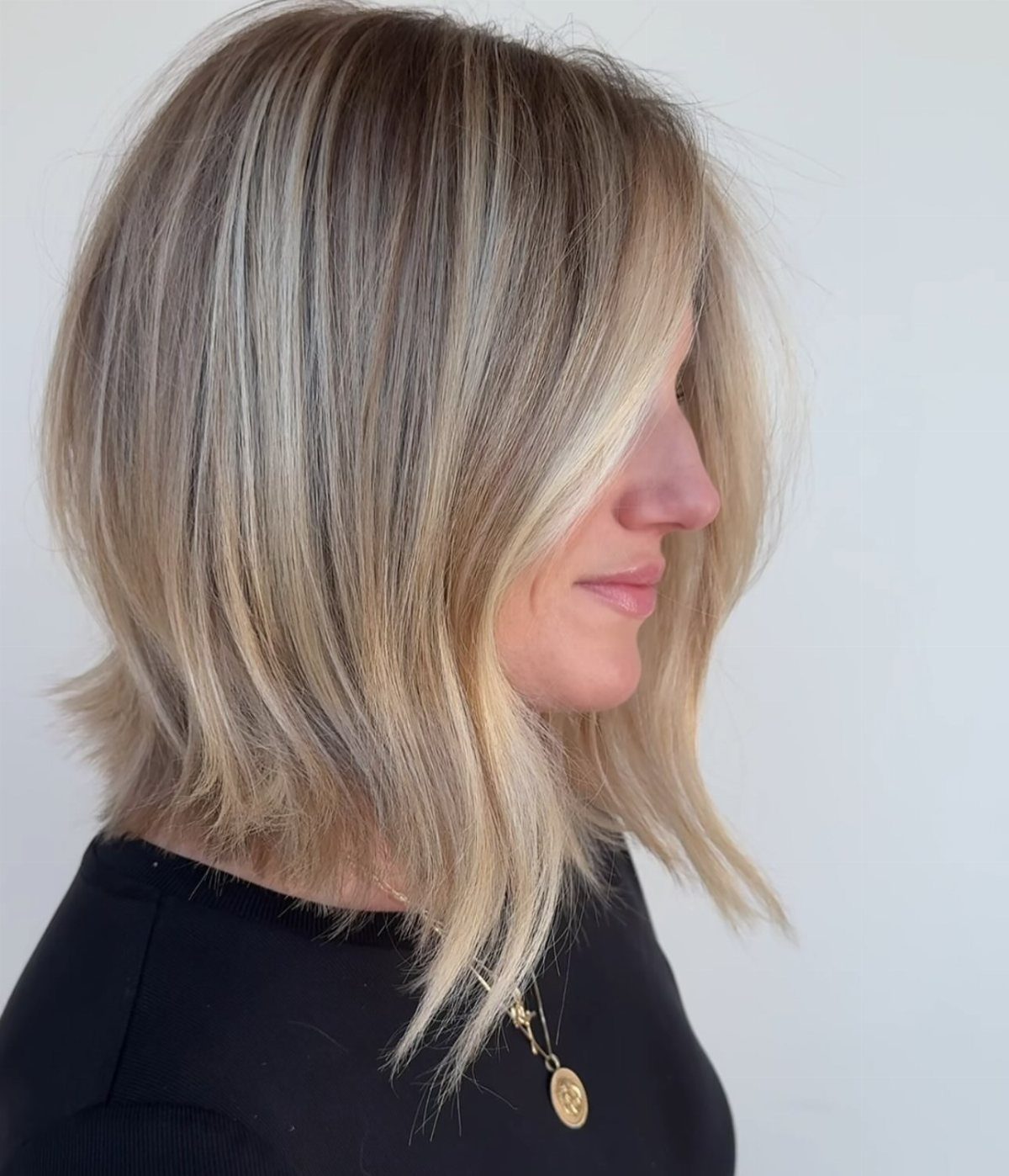 Woman with a straight blonde lob, dark roots, and softly uneven layered ends