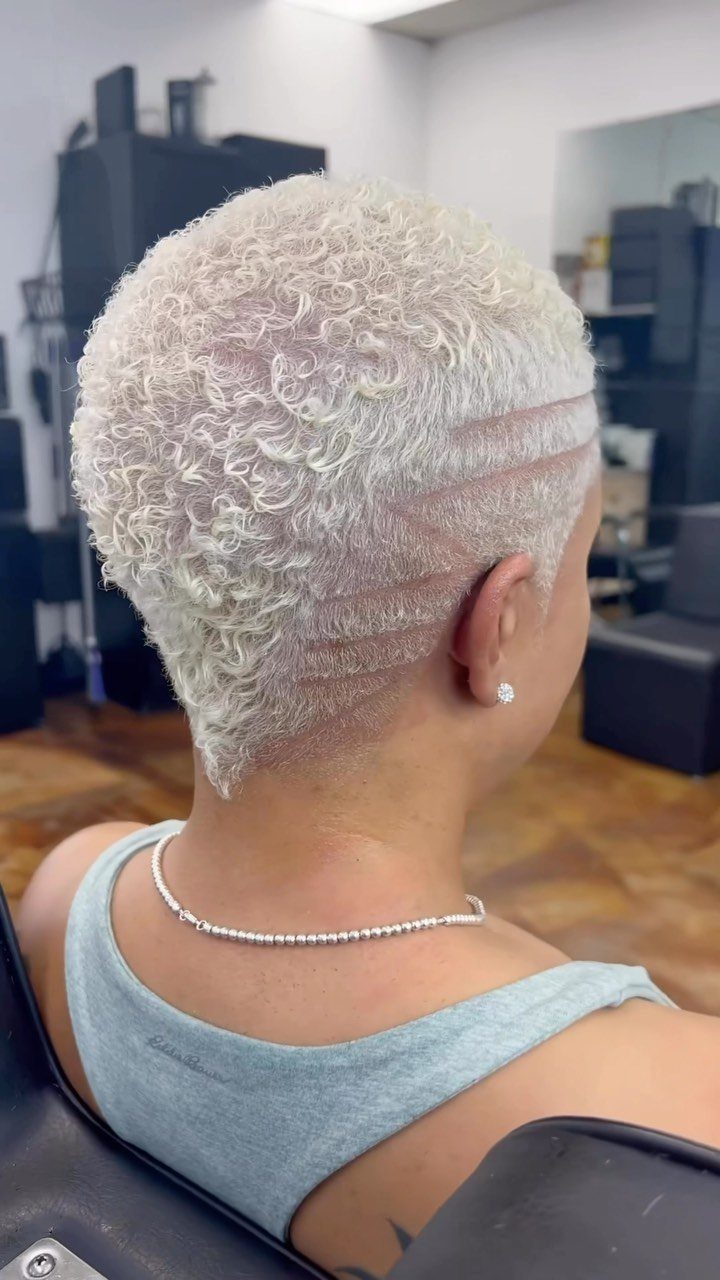 Platinum-blonde short curls with shaved horizontal lines at the nape