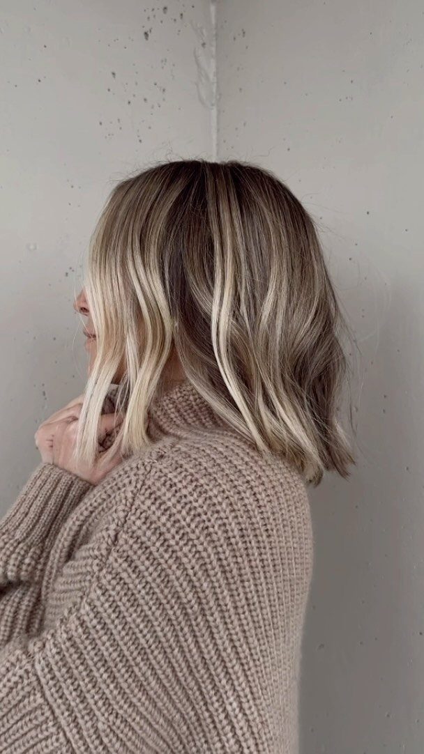 Blonde bob with dark roots fading into lighter ends against a gray wall