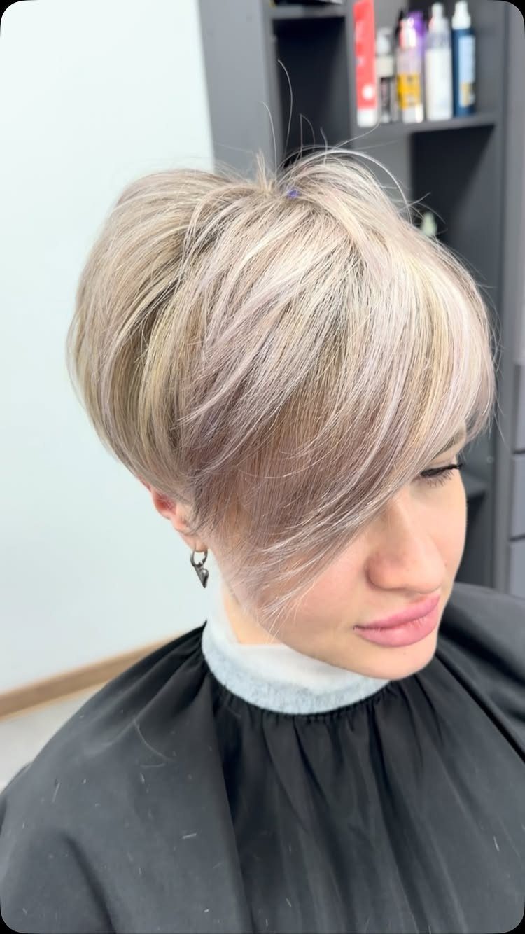 Short blonde pixie-bob with long side-swept bangs in a salon