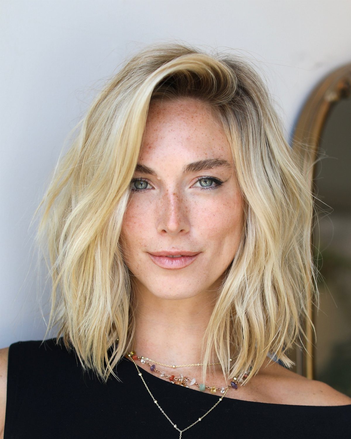 Woman with shoulder-length blonde waves wearing a black top and layered necklaces