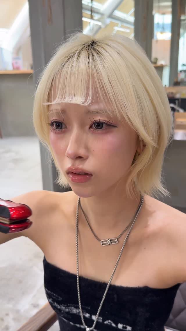 Woman with pale blonde wispy bob and bangs wearing a black strapless top