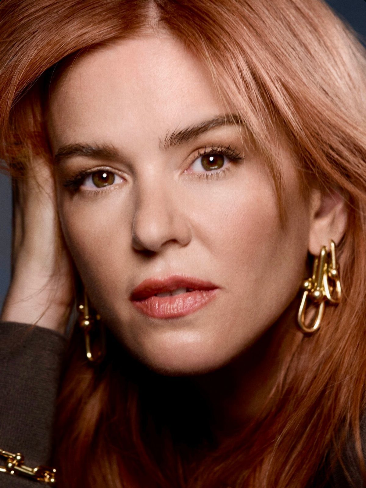 Woman with long copper-red hair and gold hoop earrings in a close-up portrait