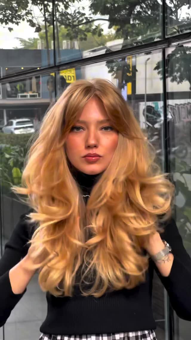 Woman displaying long, naturally warm strawberry-blonde hair with soft waves and curtain bangs