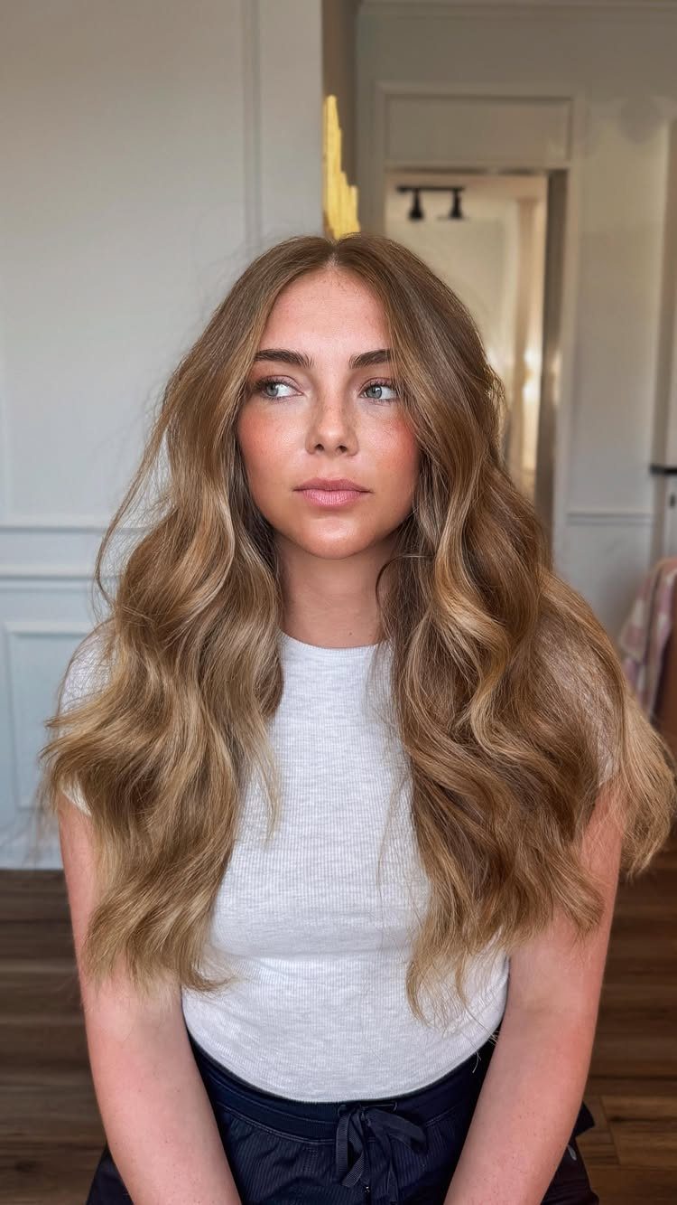 Woman displaying long wavy strawberry blonde balayage hair with blended warm highlights