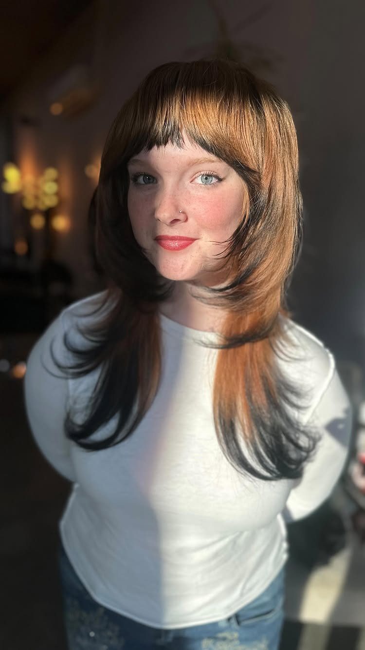 Woman with shoulder-length warm blonde hair and short bangs wearing a white top