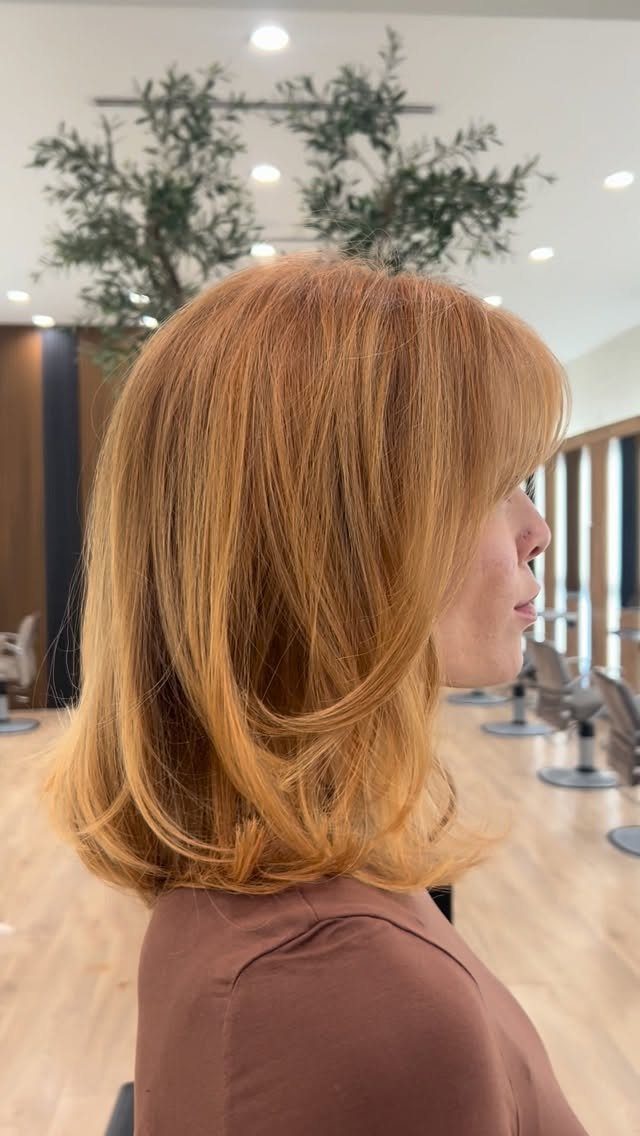 Strawberry blonde long bob with face-framing layers curled under at the ends