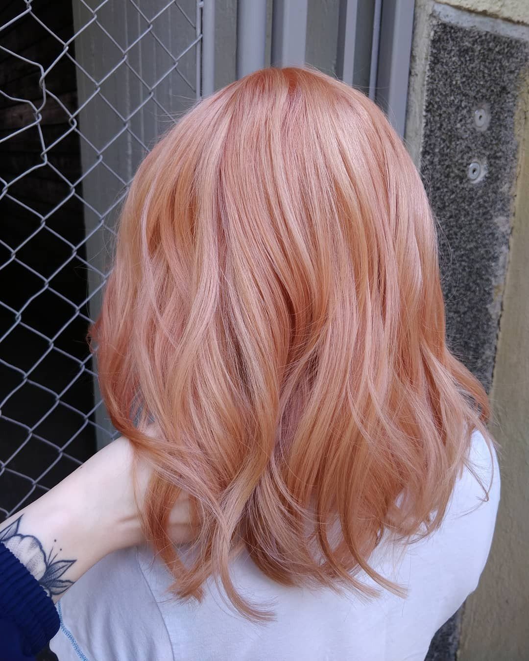 Pink strawberry-blonde curls fall over a white top beside a chain-link fence