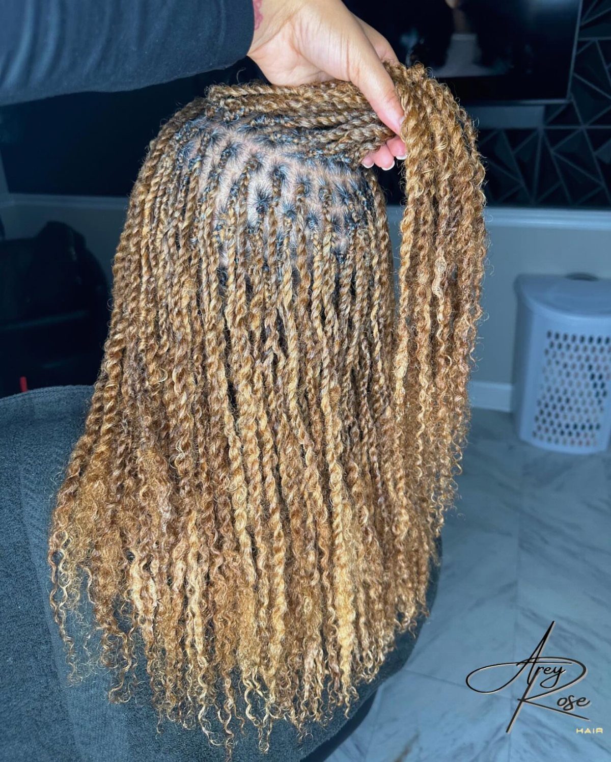 Long blonde twists hang over a dark salon cape as a hand lifts one section
