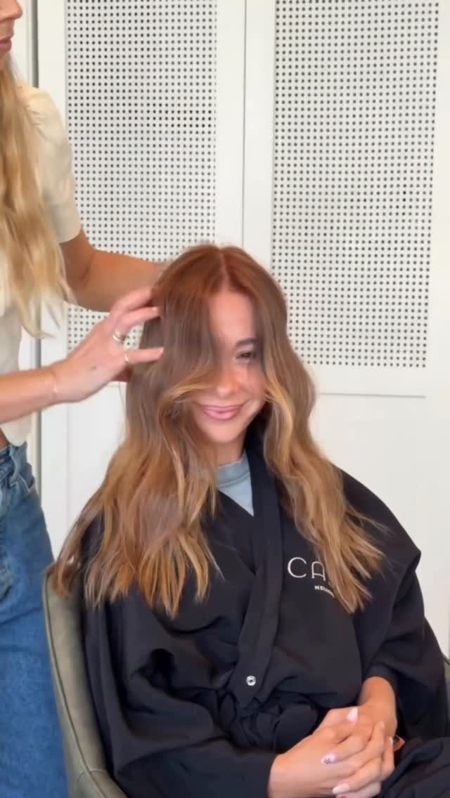 Woman displaying long wavy strawberry bronde hair during a salon styling session
