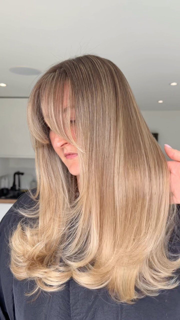 Long layered beige blonde hair with subtle honey highlights and curtain bangs