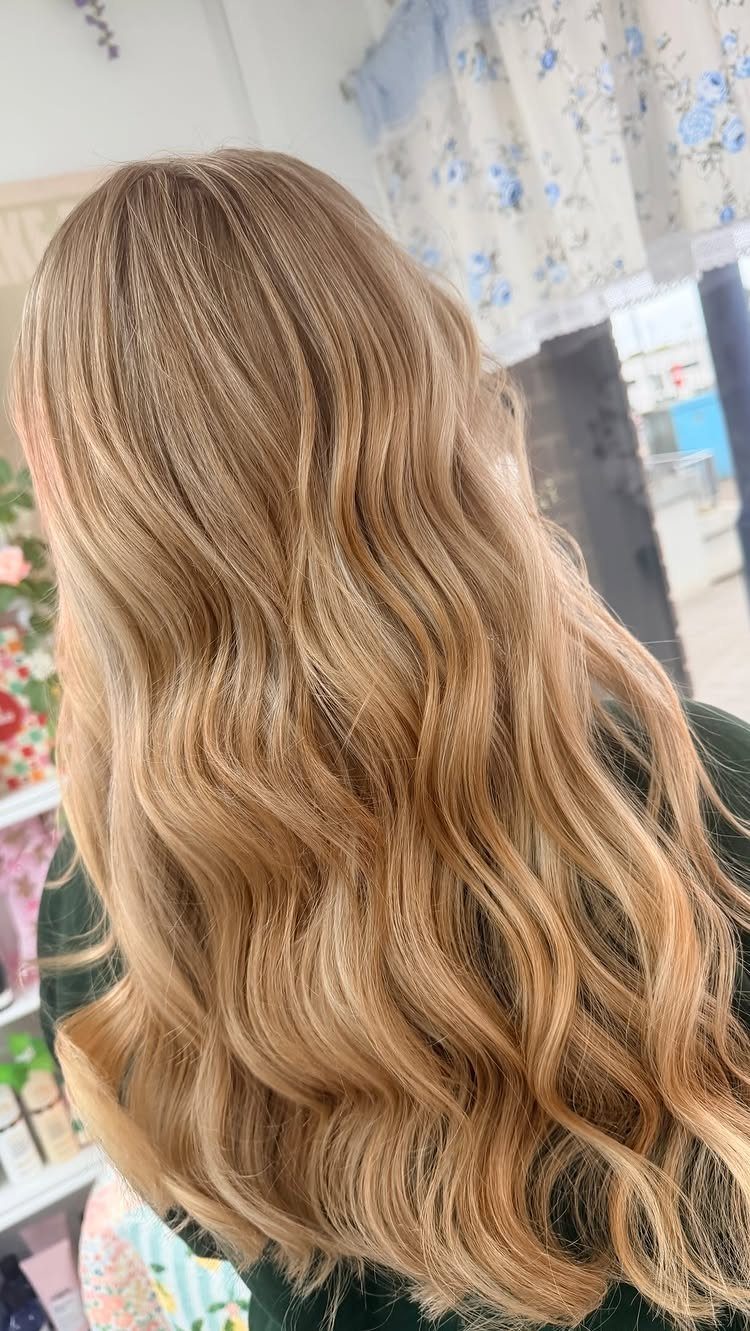 Long golden blonde hair falls in soft waves with bright, warm highlights