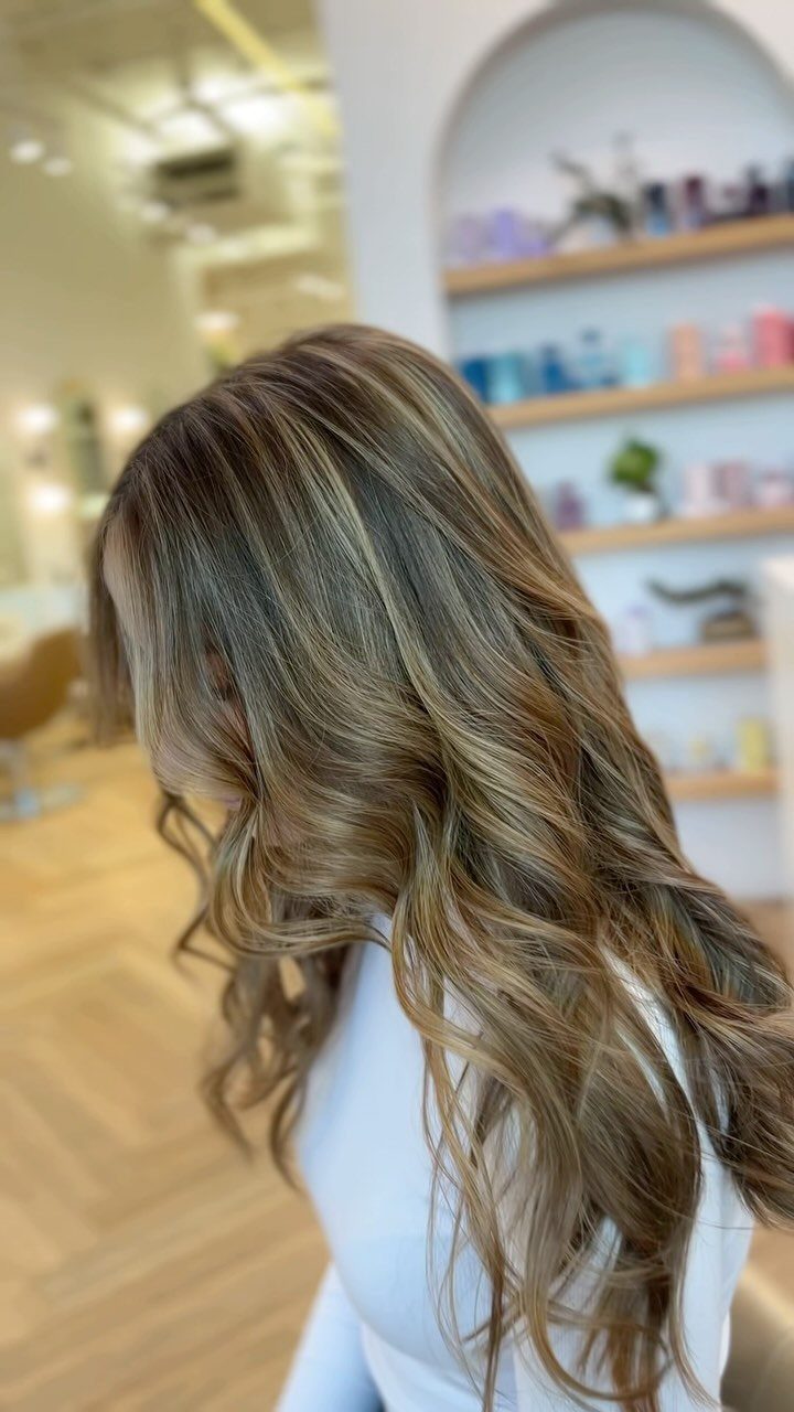 Long caramel blonde hair with soft waves and lighter highlights in a salon