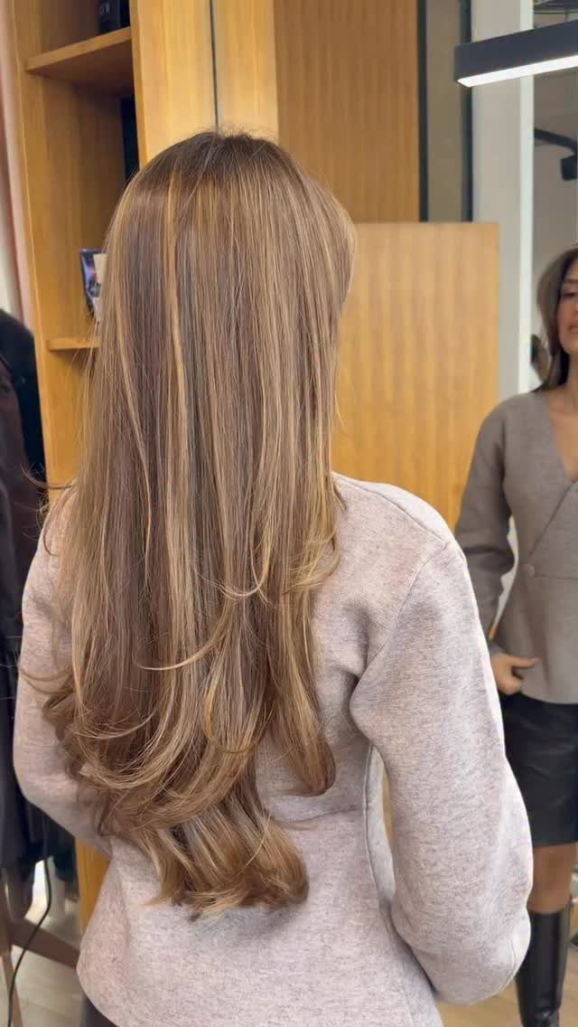 Long layered light brown hair with warm blonde highlights in a salon