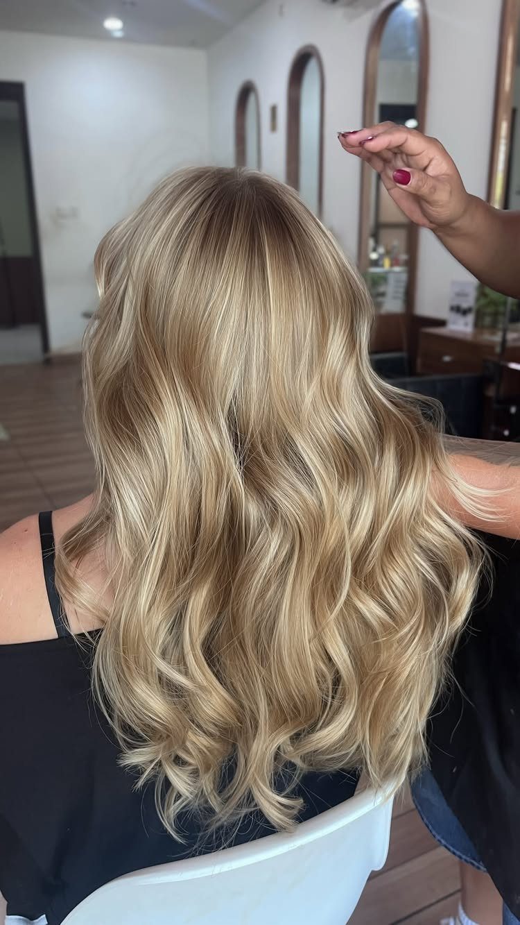 Long wavy blonde hair with layered warm tones in a salon chair