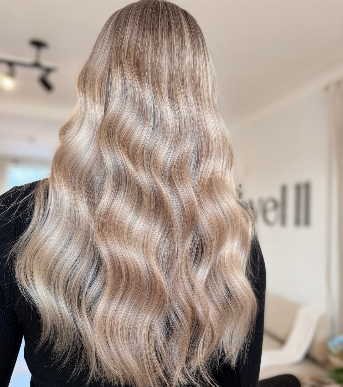 Long champagne blonde waves cascading over a black salon cape