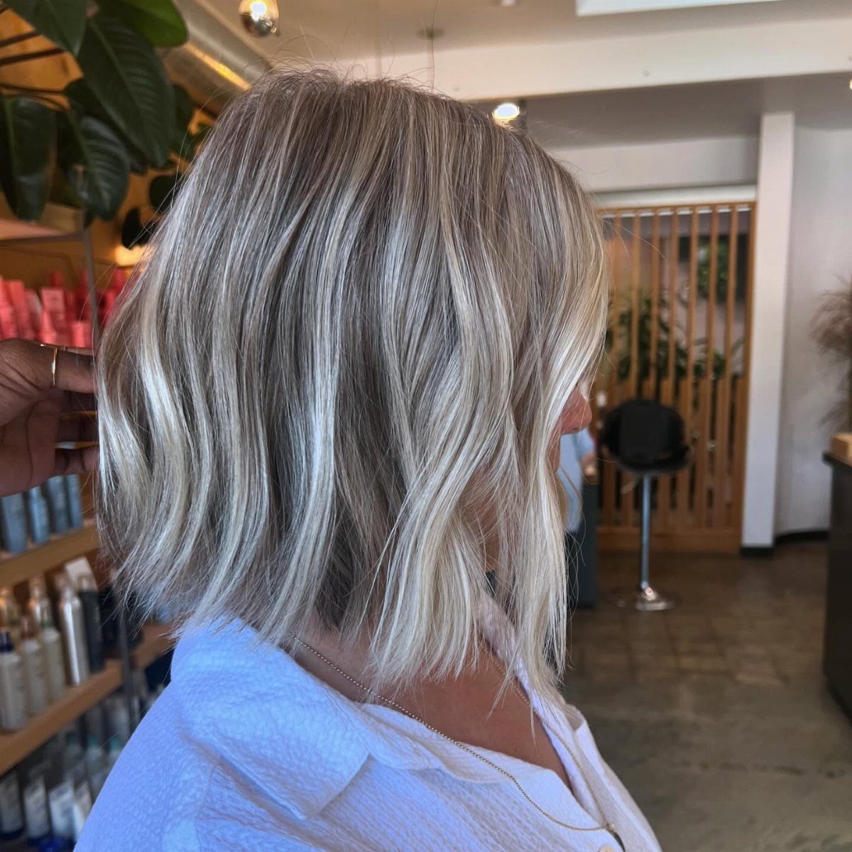 Long white-blonde hair with charcoal lowlights falls straight over a blue salon cape.