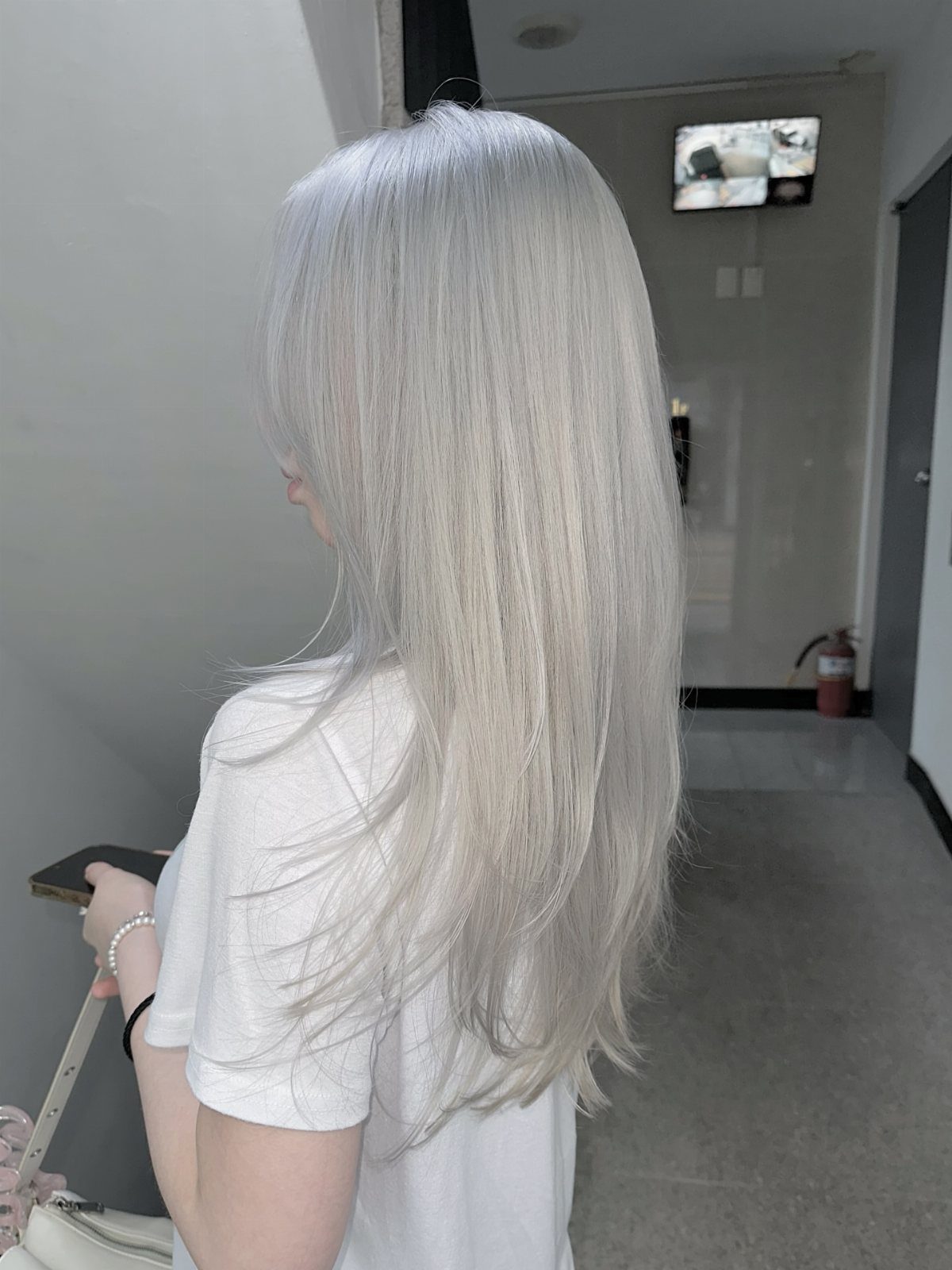 Long, sleek icy blonde hair falls straight down a person's back in a salon