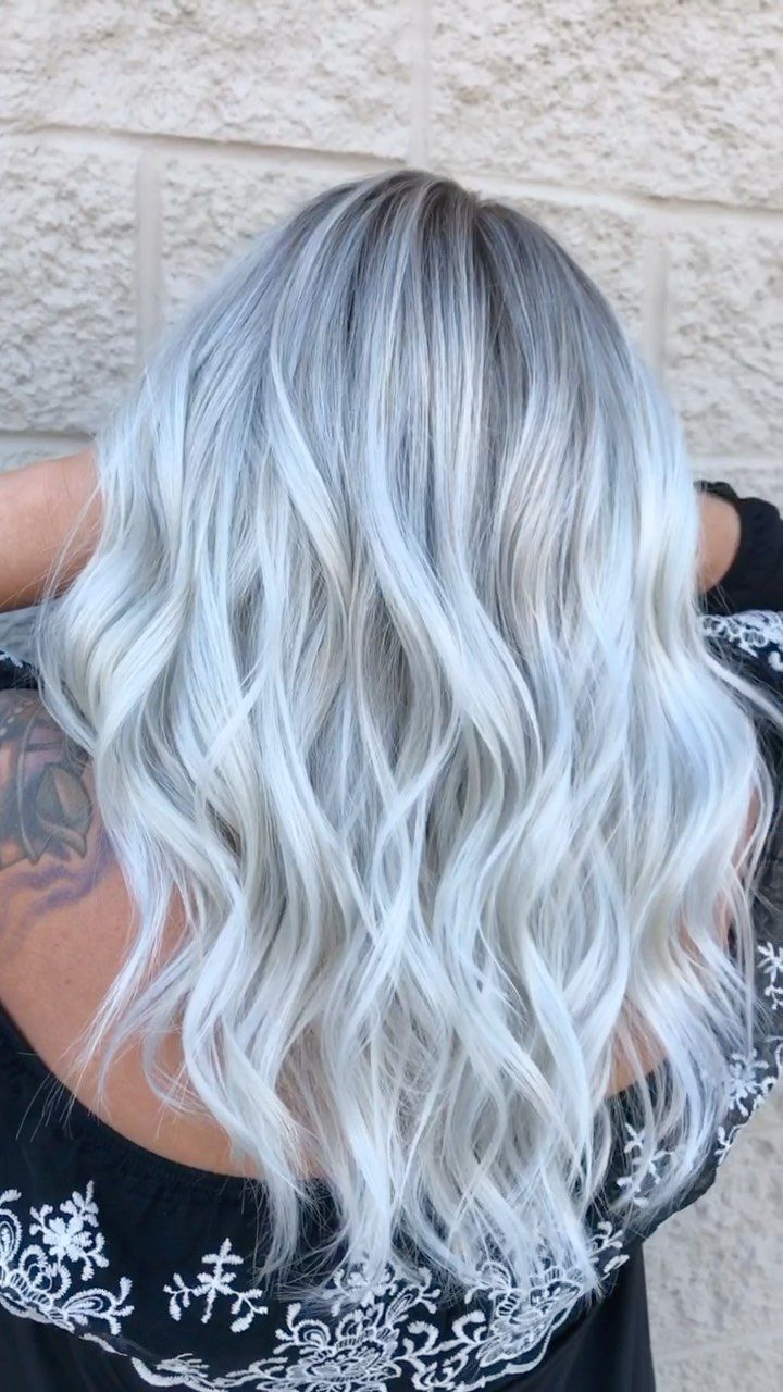 Long icy blonde hair with darker roots falls in loose waves