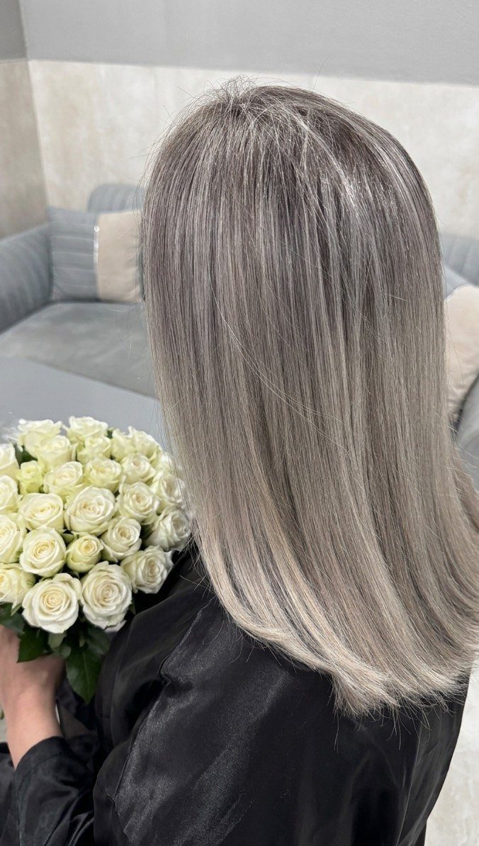 Long silver-white blonde hair with darker roots falls straight to the shoulders
