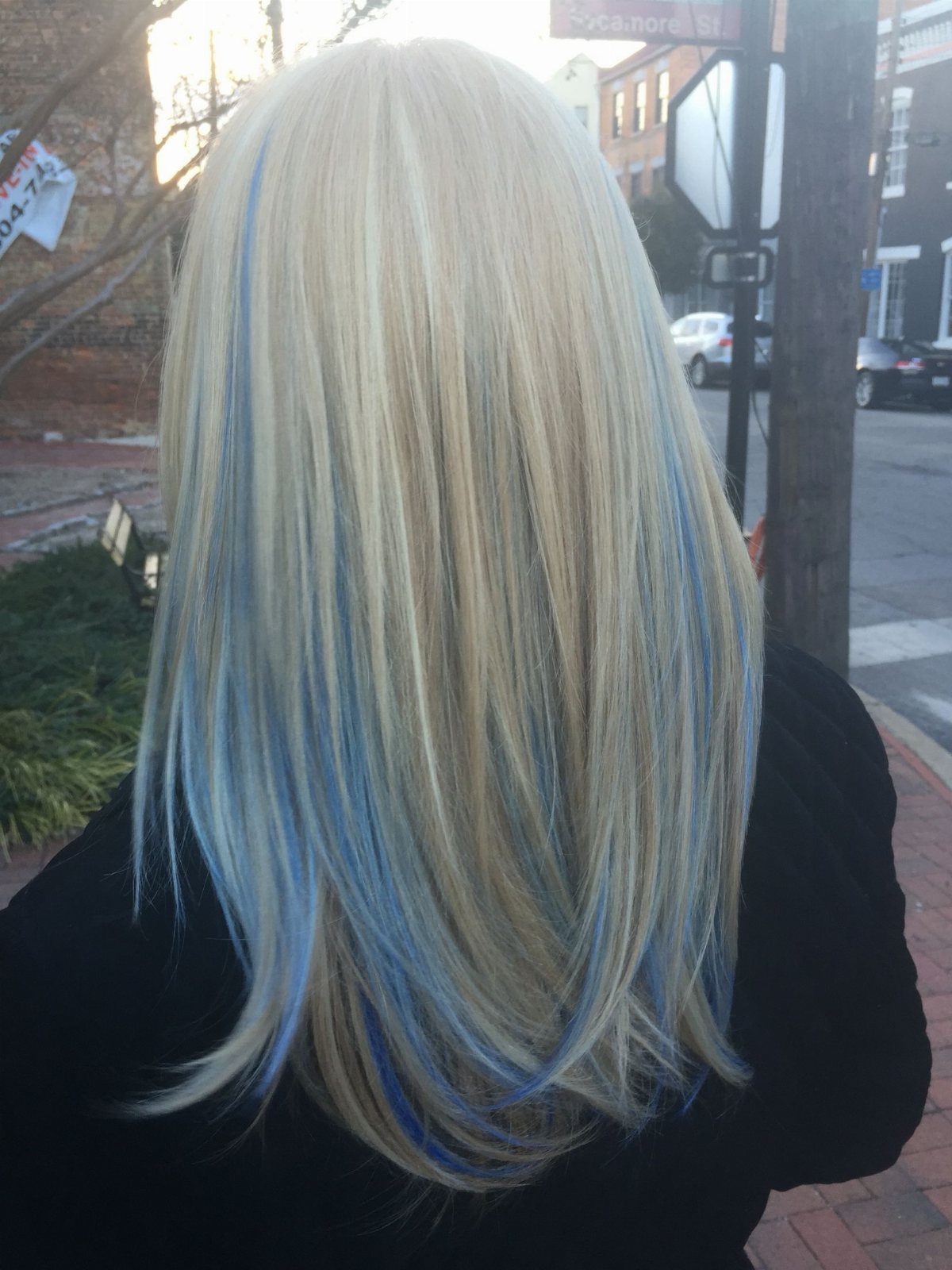 Long pale blonde hair with thin blue sections hangs straight down a black top