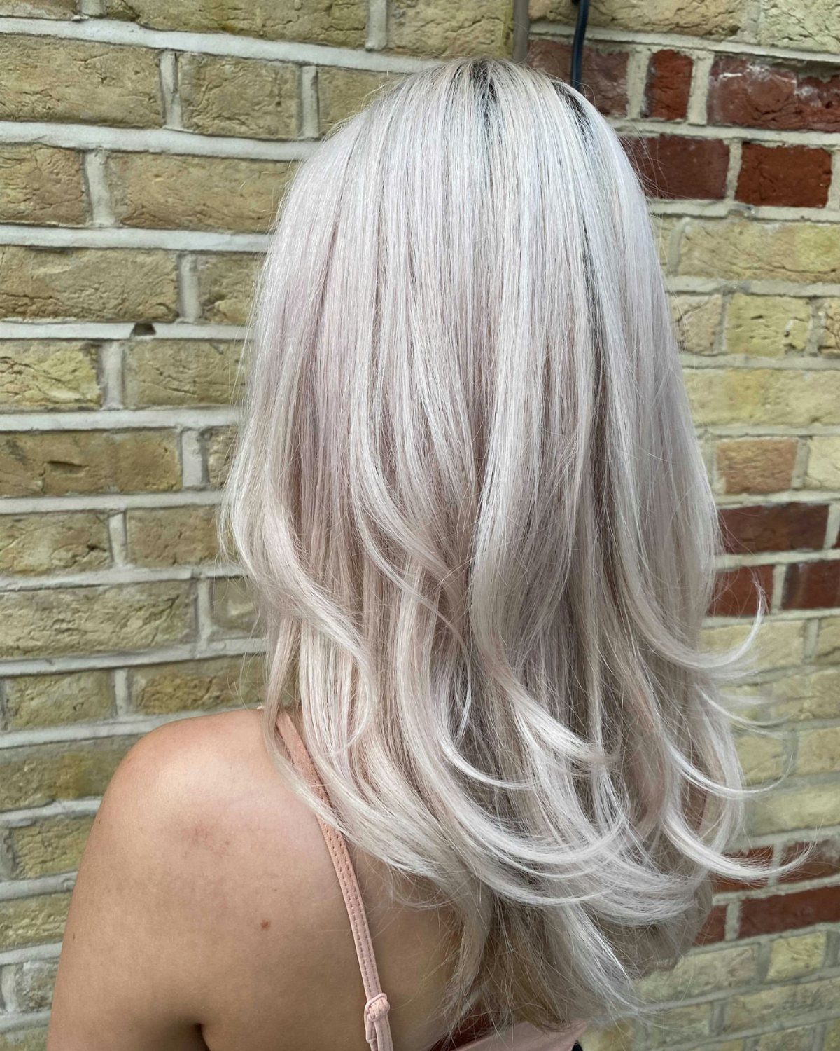 Long silver-white hair falls in smooth layers against a brick wall