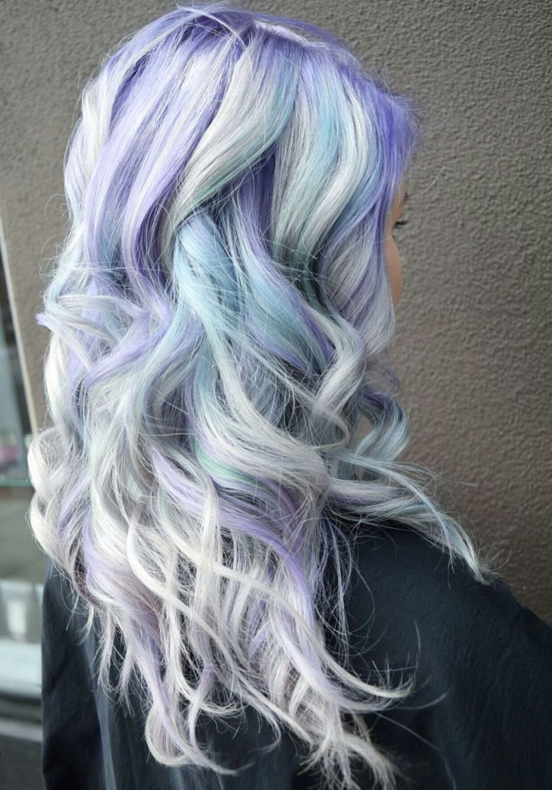 Long pale blonde curls with a subtle periwinkle tint drape over a dark top