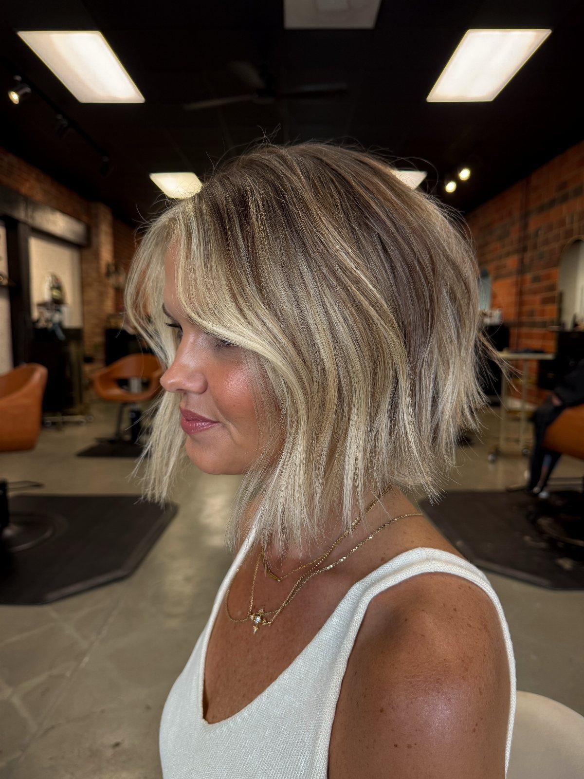 Woman showing shoulder-length sand blonde hair with darker roots in a salon