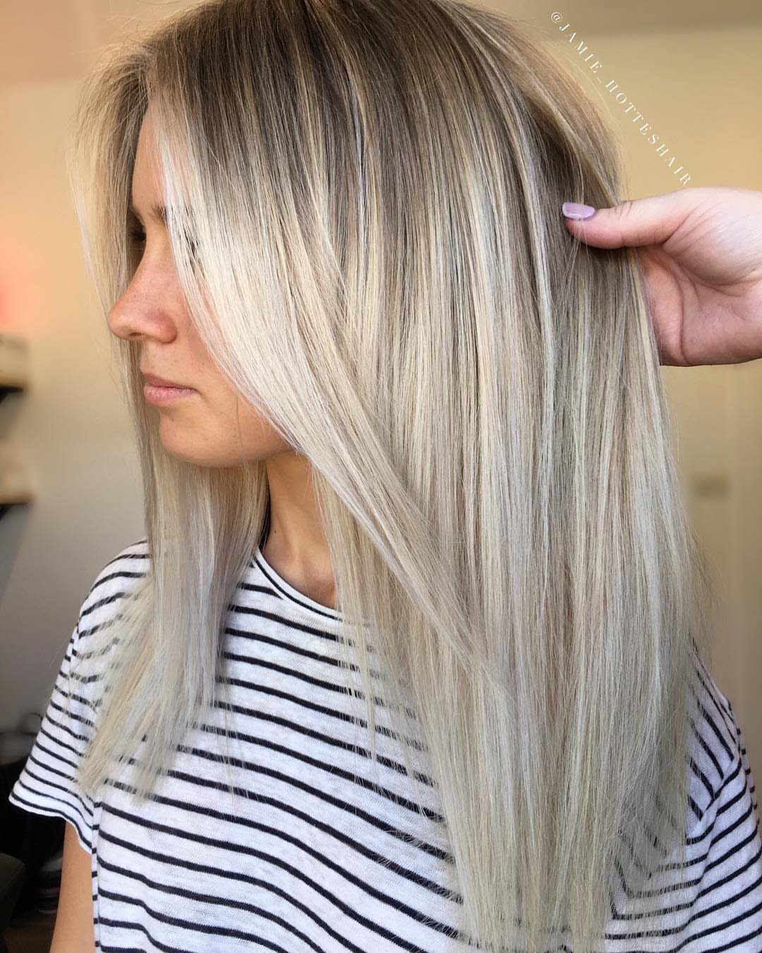 Long platinum-white hair with dark ash roots shown straight against a striped shirt