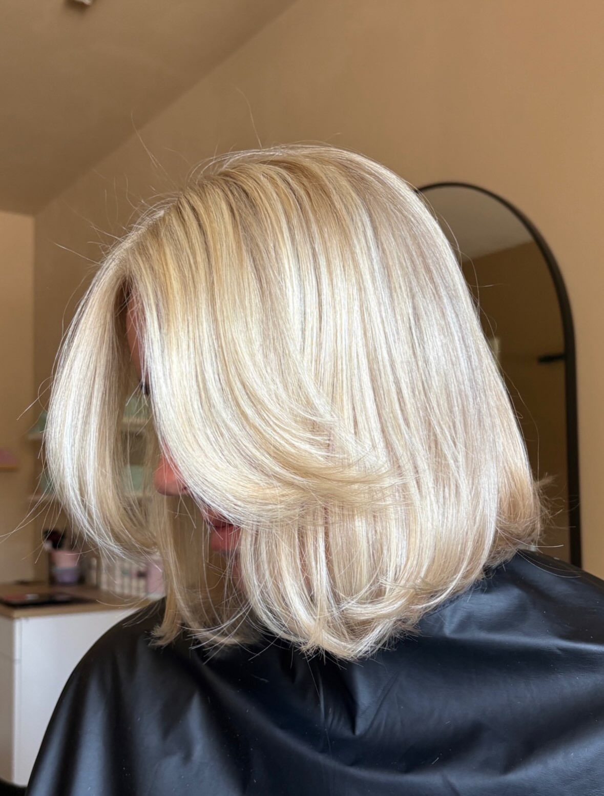 Pale blonde sleek bob with a side part and curved ends in a salon